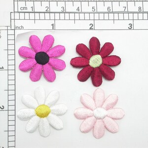 May include: Four embroidered fabric flower patches. The flowers are pink, red, white, and light pink. Each flower has a yellow center.