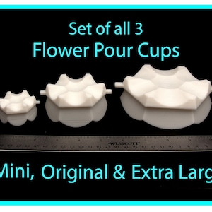 May include: Set of three white flower pour cups in different sizes: mini, original, and extra large. The cups are shown on a black surface with a ruler for scale.