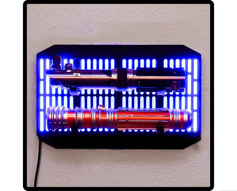 May include: Two lightsabers mounted on a black wall mount with a blue light grid background. The top lightsaber is black and silver, the bottom lightsaber is red and silver.