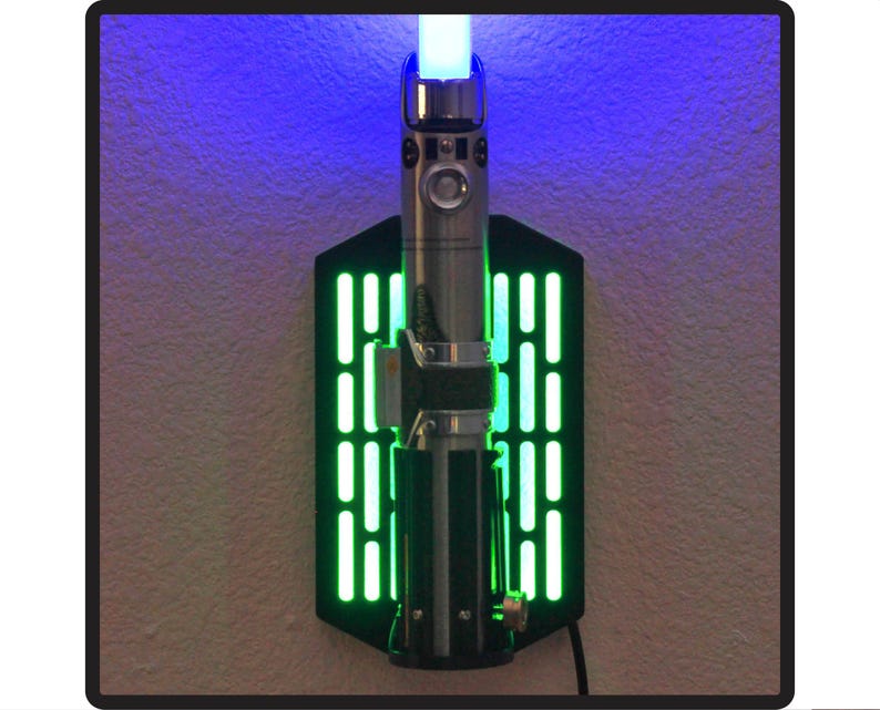 May include: A black wall mount with a green light display and a silver lightsaber replica mounted in the center. The lightsaber is lit with a blue light.