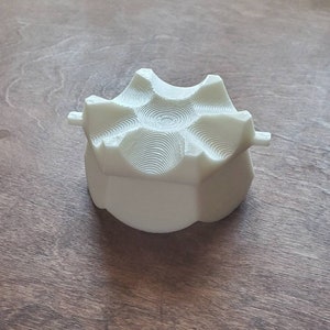 May include: A white, 3D printed, hexagonal-shaped object with a textured, circular design on the top.