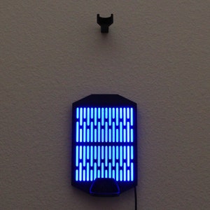 May include: A black wall-mounted light fixture with a blue light that creates a grid pattern. The light is on and illuminating the wall.