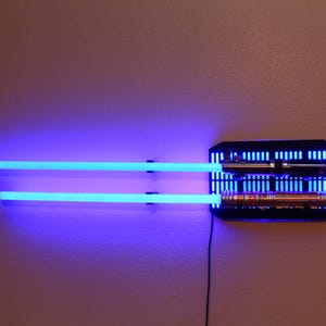 May include: Two blue lightsabers mounted on a black wall mount with two lightsabers in the mount. The lightsabers are illuminated with blue light.