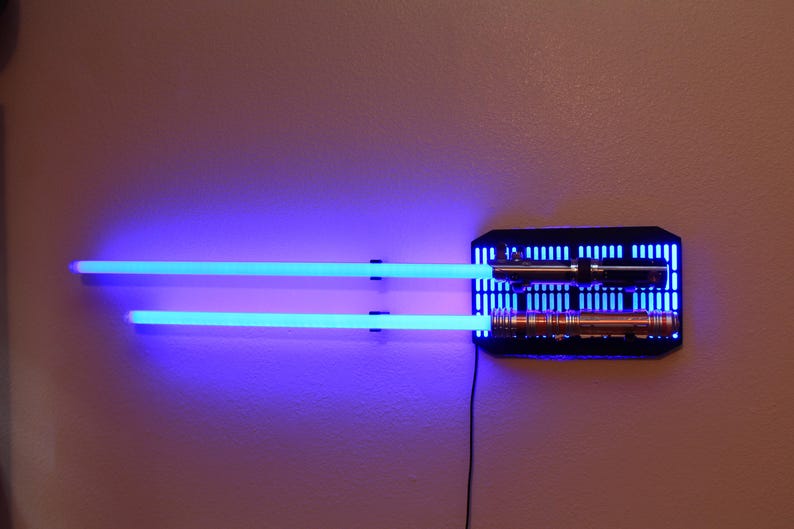 May include: Two blue lightsabers mounted on a black wall mount with two lightsabers in the mount. The lightsabers are illuminated with blue light.