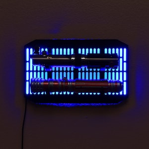 May include: A black wall mount with blue LED lights displaying two lightsabers. The lightsabers are a black and a red color.