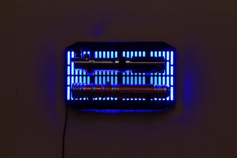 May include: A black wall mount with blue LED lights displaying two lightsabers. The lightsabers are a black and a red color.