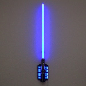 May include: A blue lightsaber wall mount with a black base and a silver handle. The lightsaber is lit up and the blade is a bright blue color.