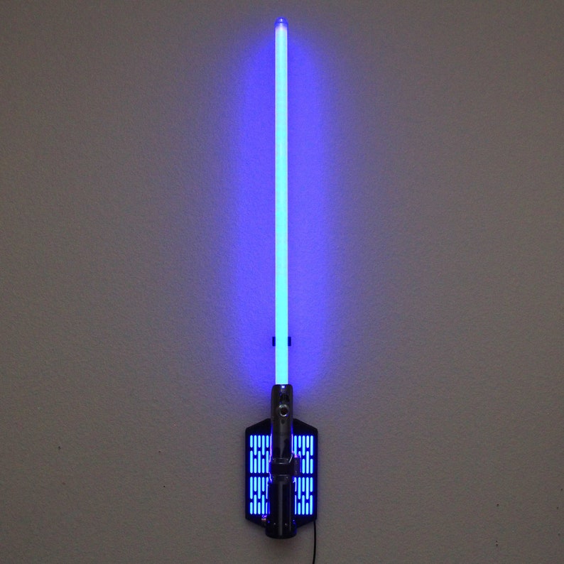 May include: A blue lightsaber wall mount with a black base and a silver handle. The lightsaber is lit up and the blade is a bright blue color.