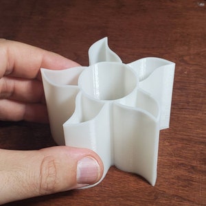 Puede incluir: Organizador de plástico blanco impreso en 3D con cinco compartimentos en forma de estrella. El organizador está diseñado para guardar objetos pequeños como bolígrafos, lápices u otros artículos de oficina.
