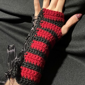 Könnte beinhalten: Rote und schwarze gestreifte Fingerlose Handschuhe aus Häkelarbeit mit einem schwarzen Spitzenband-Detail.