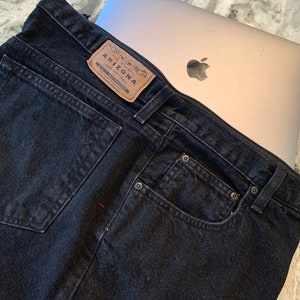 May include: Black denim jeans with a brown leather patch that says "The Original Arizona Jean Company" and a laptop computer inside the pocket.