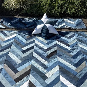 May include: A denim quilt with a herringbone pattern in various shades of blue. A star-shaped pillow with white and blue segments rests on the quilt. Two matching denim pillowcases are also visible.