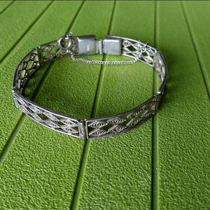 Könnte beinhalten: Ein silbernes Filigranarmband mit einem zarten Kettenverschluss. Das Armband besteht aus filigranem, ineinander verschlungenem Silberdraht, der ein zartes und elegantes Design erzeugt.