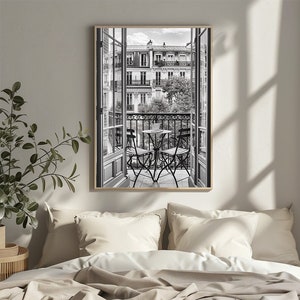 Könnte beinhalten: Schwarzweißfoto eines Pariser Balkons mit einem kleinen Tisch und zwei Stühlen. Der Balkon blickt auf eine Straße mit Gebäuden im Hintergrund.