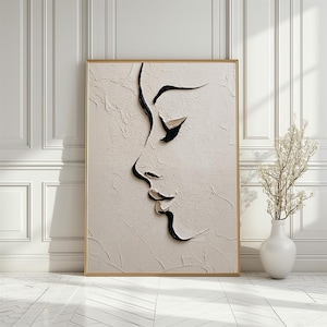 May include: A framed abstract artwork depicting a face profile. Black lines define the facial features on a textured, off-white background. The frame is a light gold colour. A white vase with dried flowers is to the right.