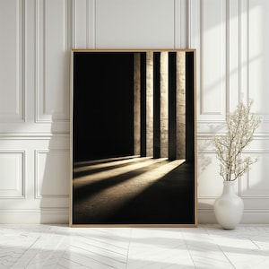 May include: A framed art print featuring a dark interior with three vertical columns. Sunlight streams through the columns, casting shadows on the floor. The artwork is in a gold frame, and the background is a white wall with a vase and decorative plant.