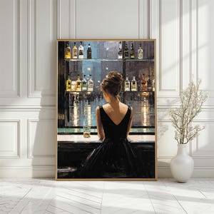 May include: A framed art print depicts a woman in a black dress at a bar, facing away from the viewer. The bar is stocked with bottles, and a glass sits on the counter. The artwork has a gold frame and is displayed against a white wall.