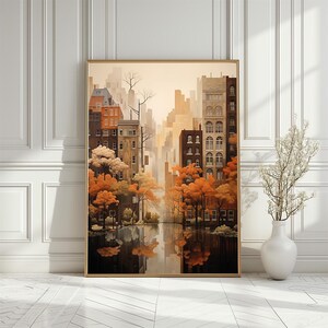May include: Framed art print showing a cityscape with buildings and trees in autumnal hues. The artwork features a reflection of the city in water. The colour palette includes shades of orange, brown, and beige.