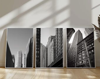 May include: Set of three framed black and white prints featuring urban cityscapes. The images showcase tall buildings and architectural details, creating a modern and artistic aesthetic. The prints are displayed on a wooden floor.