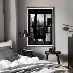 K&ouml;nnte beinhalten: Schwarz-Wei&szlig;-Druck eines Stadtbildes, das durch ein Fenster betrachtet wird. Der Fensterrahmen ist schwarz, und die Geb&auml;ude sind hoch und dicht beieinander. Der Druck befindet sich in einem Schlafzimmer mit einer schwarzen Lampe und Beistelltischen.