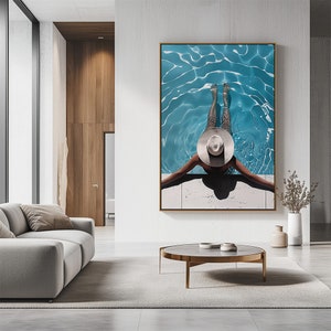 May include: A woman wearing a white hat sits on the edge of a blue swimming pool with rippling water. The woman's legs are in the water and her arms are outstretched.