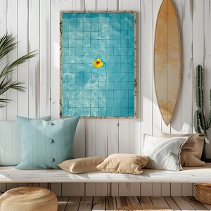 May include: A framed print featuring a vibrant blue pool with a yellow rubber duck floating in the center. A surfboard and cactus are mounted on a white wood-paneled wall. Decorative pillows and a woven basket complete the coastal theme.