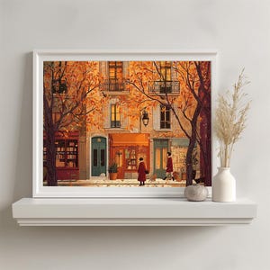 May include: A framed art print showing a European street scene in autumn. The artwork features buildings with orange awnings and trees with orange leaves. Two figures in red coats walk down the street. The print is displayed on a white shelf.