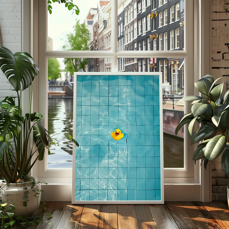 May include: A framed print featuring a top-down view of a swimming pool with blue tiles and a yellow rubber duck floating in the water. The print is displayed in front of a window overlooking a canal and buildings.