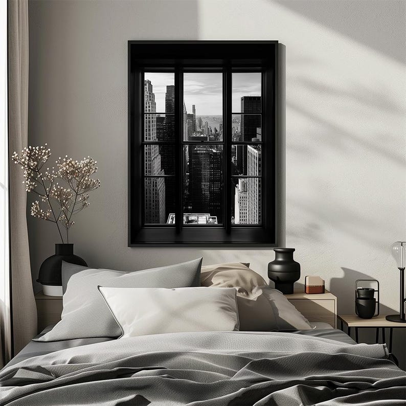 K&ouml;nnte beinhalten: Schwarz-Wei&szlig;-Druck eines Stadtbildes, das durch ein schwarzes Fenster betrachtet wird. Der Druck h&auml;ngt &uuml;ber einem Bett mit grauer Bettw&auml;sche und Kissen. Links im Bild befindet sich eine schwarze Vase mit Blumen.