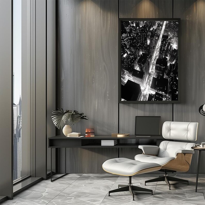 May include: A black and white photograph of a city at night, framed and hanging on a dark gray wall. The photo shows a street with buildings and lights. A white leather armchair and ottoman are in the foreground.