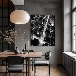 May include: A black and white photograph of a city skyline at night, with street lights illuminating the roads. The photo is framed and hanging on a gray wall above a wooden dining table with four chairs.