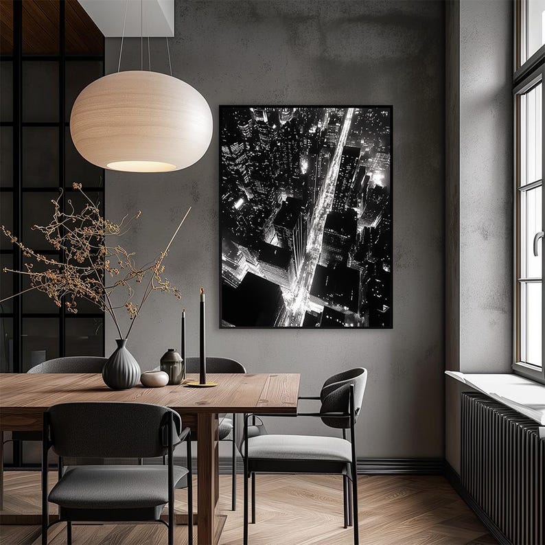 May include: A black and white photograph of a city skyline at night, with street lights illuminating the roads. The photo is framed and hanging on a gray wall above a wooden dining table with four chairs.