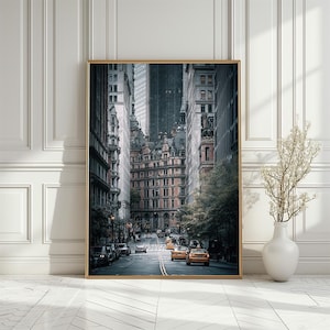May include: A framed print depicting a city street. The image shows a view down a street flanked by tall buildings. The buildings display various architectural styles, some with intricate details. Yellow taxis and other vehicles are visible on the road.