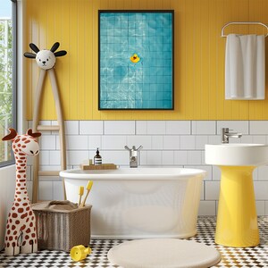 May include: A bright bathroom scene with a white bathtub, sink, and towel rack against yellow and white tiled walls. A framed picture of a pool with a rubber ducky hangs above the tub. A giraffe toy and a basket with toothbrushes are in the foreground.