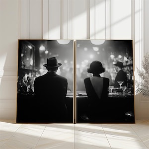 May include: Two framed black and white prints depict a vintage bar scene. One shows a man in a fedora at the bar, the other a woman in a dress. The prints have gold frames and are set against a white wall.