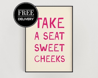 Może przedstawiać: Oprawiony wydruk artystyczny z napisem "TAKE A SEAT SWEET CHEEKS" w jaskraworóżowych literach na kremowym tle. Czarny okrąg z napisem "FREE DELIVERY" znajduje się w lewym górnym rogu.