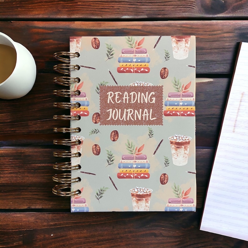 May include: A spiral bound reading journal with a light blue cover featuring a repeated pattern of coffee cups, books, and coffee beans. The text "READING JOURNAL" is printed in brown on a tan rectangle in the centre of the cover.