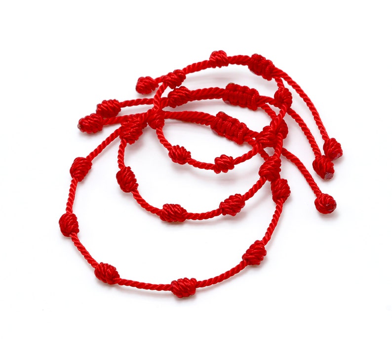 Op de afbeelding: Drie rode geknoopte armbanden op een witte achtergrond. Elke armband is gemaakt van rood koord en heeft meerdere knopen. De armbanden vari&euml;ren enigszins in grootte en zijn gelaagd gerangschikt.
