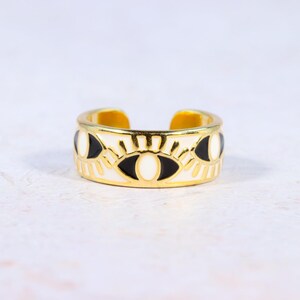 Puede incluir: Anillo ajustable dorado con una banda blanca con dise&ntilde;os de ojos negros y blancos. El anillo tiene un acabado pulido y una est&eacute;tica minimalista. El anillo mide aproximadamente 1,9 cm de ancho, adecuado para el uso diario.