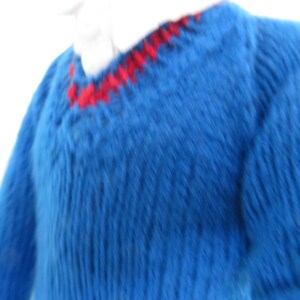 May include: A blue knitted jumper featuring a V-neckline with a red stitched trim detail. The garment is crafted with a ribbed texture throughout the body and sleeves, and it is worn over a white collared shirt visible at the neckline.
