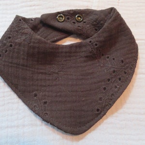 May include: A brown cotton baby bib with a delicate embroidered design and two small buttons.