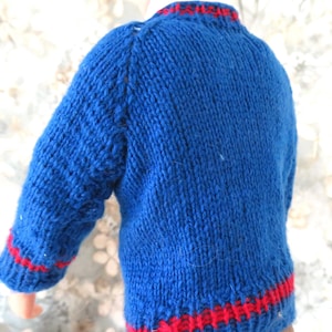 May include: A hand-knitted blue jumper with long sleeves, featuring a ribbed crew neckline and a ribbed hem. The jumper is accented with a thin horizontal red stripe around the collar, the cuffs of the sleeves, and the bottom hemline.