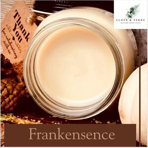 May include: A jar of cream-colored product with the word "Frankensense" at the bottom. The jar is open, revealing the smooth contents. A small tag with the words "Thank You" is visible, along with a pine cone.