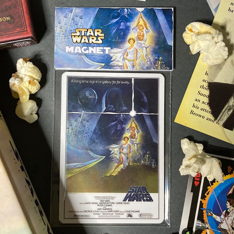 K&ouml;nnte beinhalten: Ein Star Wars Magnet mit dem Filmposter. Der Magnet zeigt das Star Wars Logo und den Titel. Das Kunstwerk zeigt Luke Skywalker, Prinzessin Leia und Darth Vader. Der Text "Vor langer Zeit in einer weit, weit entfernten Galaxie..." ist ebenfalls sichtbar.