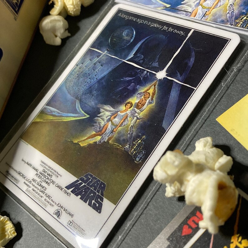 K&ouml;nnte beinhalten: Ein Star Wars-Filmplakat mit Luke Skywalker und Prinzessin Leia, mit dem Todesstern und Darth Vader im Hintergrund. Das Plakat enth&auml;lt den Text "Vor langer Zeit in einer weit, weit entfernten Galaxie..." und das Star Wars-Logo.