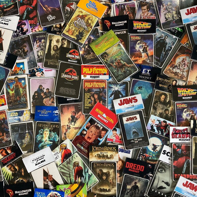 K&ouml;nnte beinhalten: Eine Sammlung von Magneten mit Filmthemen, darunter Titel wie "Jurassic Park", "Pulp Fiction" und "Zur&uuml;ck in die Zukunft". Die Magnete zeigen farbenfrohe Filmplakate, wobei das Wort "Magnet" auf vielen zu sehen ist. Eine Vielzahl von Genres sind vertreten.
