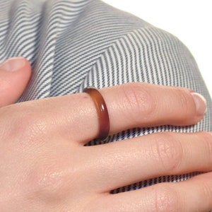 Peut inclure: Gros plan d'une main portant une bague brune. La bague est simple et élégante, avec une finition lisse et polie.