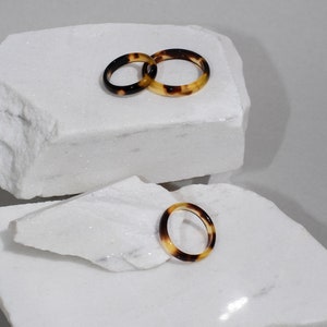 Peut inclure: Trois bagues en écaille de tortue sur une surface en marbre blanc. Les bagues sont fines et présentent un motif brun et jaune.