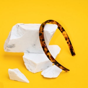 May include: A brown and black tortoiseshell headband on a white rock against a yellow background.
