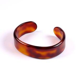 Può includere: Un braccialetto rigido in plastica marrone effetto tartaruga.